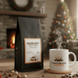 Hazelnut coffee bag and steaming mug on a table with a Christmas tree and fireplace in the background