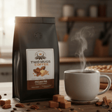 Two Mugs Coffee bag with a steaming mug on a wooden table, surrounded by coffee beans and pecans.